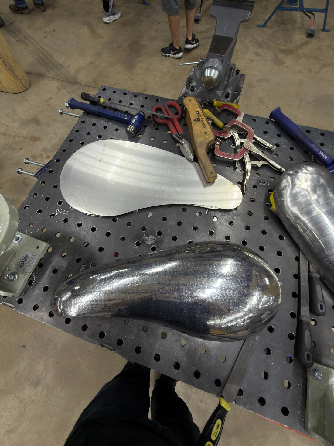 Flat aluminum blank beside hand-hammered teardrop-shaped aluminum panels