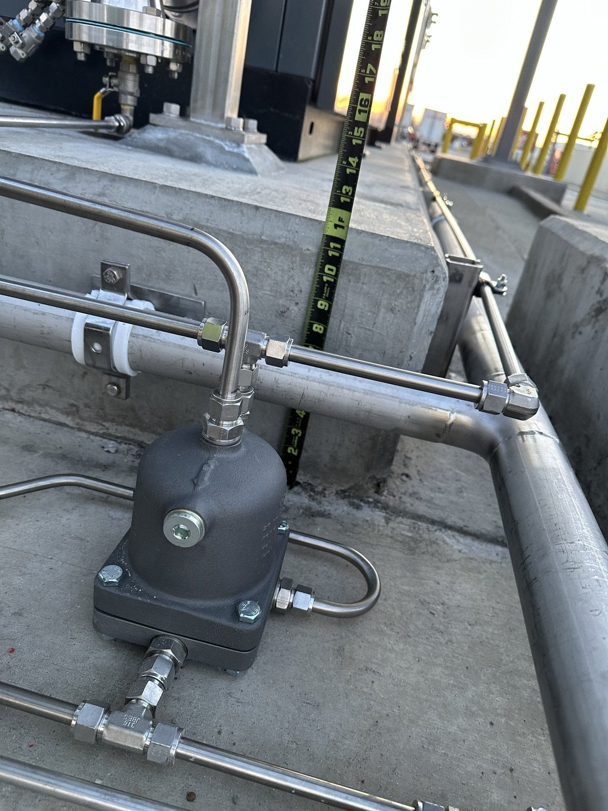 Close-up of stainless steel instrument tubing with compression fittings feeding a gray cast valve body, beside a welded stainless pipe elbow